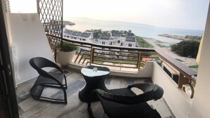 A balcony with two wicker chairs and a small table, overlooking a coastal area with buildings and a beach. - Jounieh Cozy Apartment With Sea View (Jounieh)