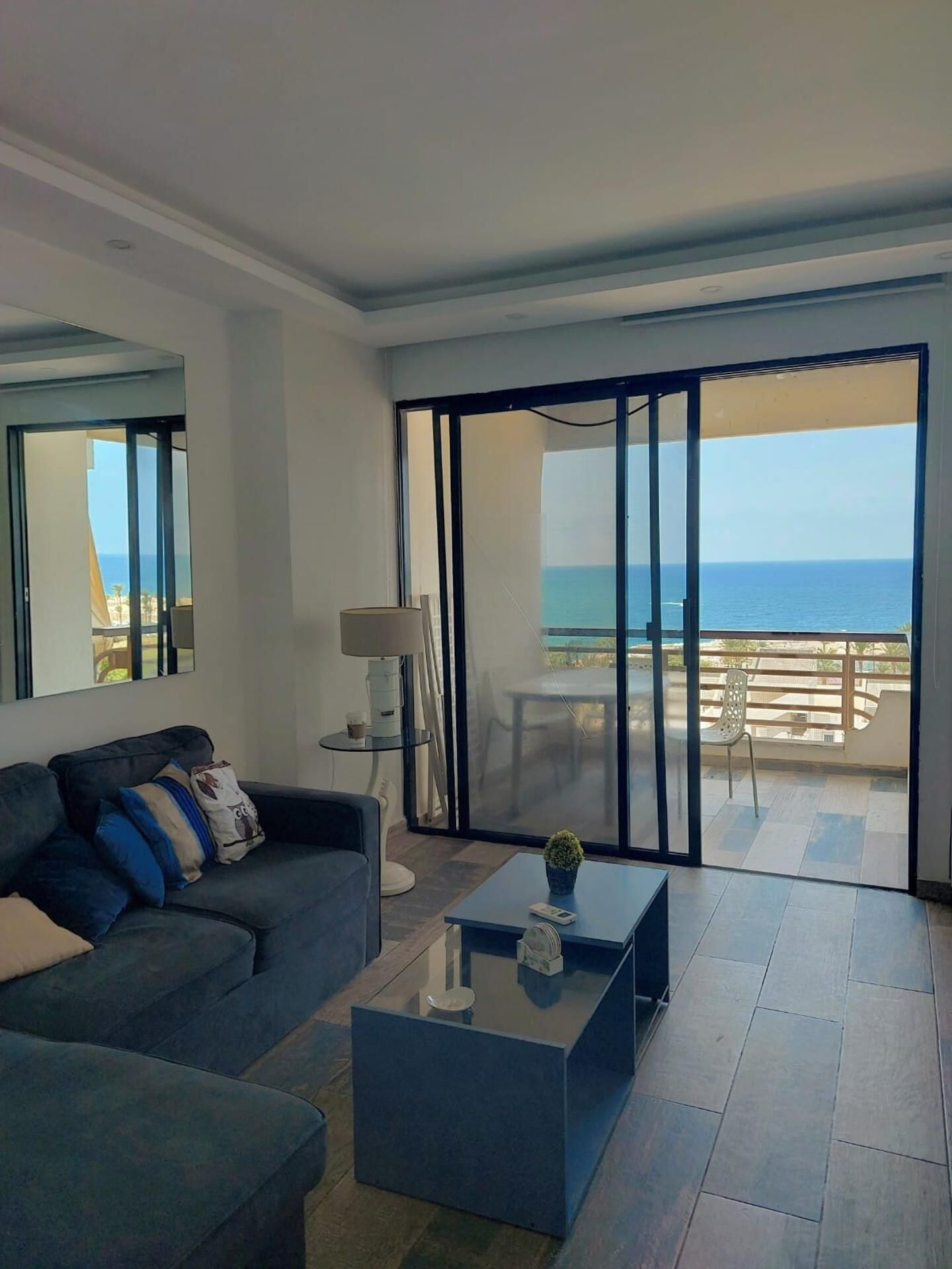 Una sala de estar moderna con un sofá, una mesa de centro y vistas al océano a través de puertas correderas grandes.