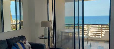 Una sala de estar moderna con un sofá, una mesa de centro y vistas al océano a través de puertas correderas grandes.