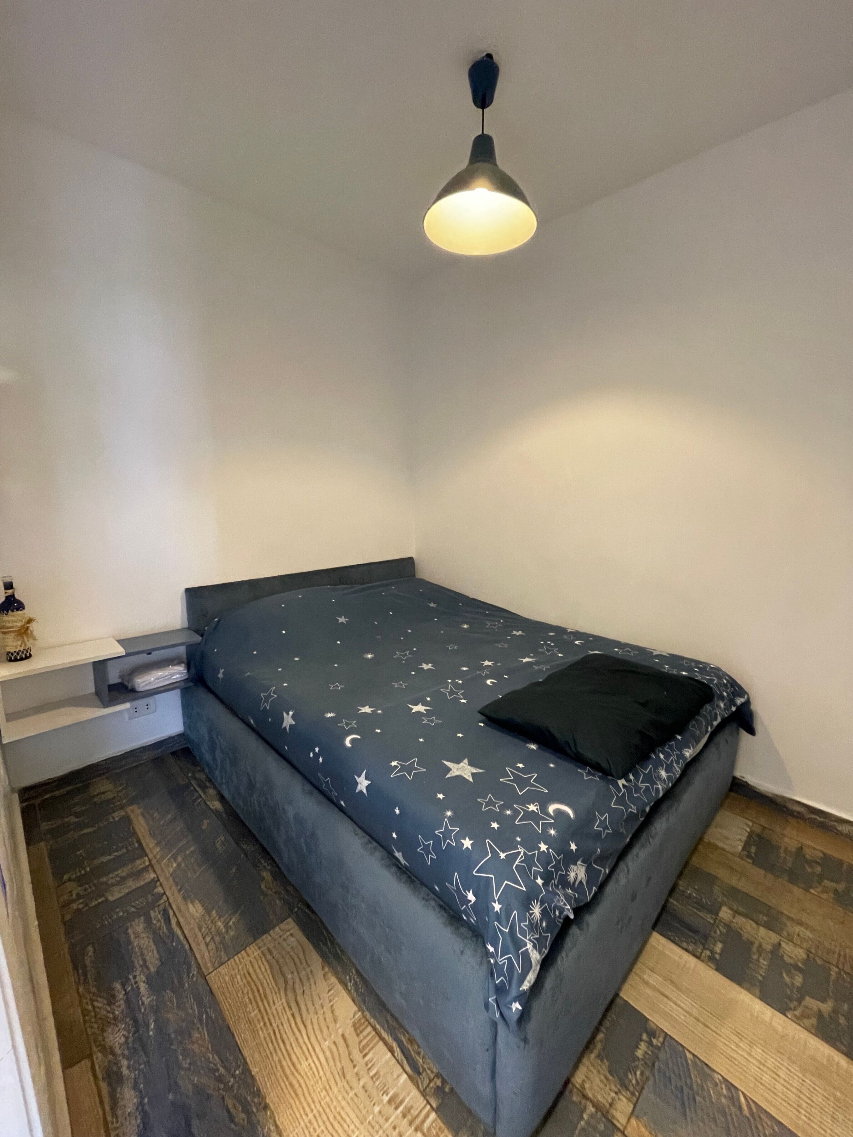 A bedroom with a bed, a nightstand, and a hanging light fixture.