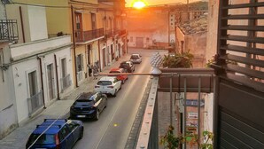 Straßenansicht bei Sonnenuntergang mit Gebäuden an beiden Seiten, einem klaren Himmel und parkenden Autos am Straßenrand.