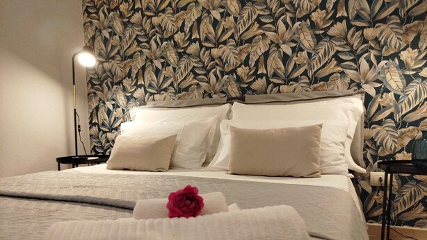 Ein ordentlich bezogenes Bett mit weißer Daunendecke, zwei Kissen und einem gefalteten Handtuch mit Rosenmotiv.
