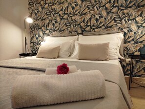 A neatly made bed with a white duvet, two pillows, and a folded towel with a rose.