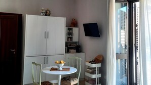 Ein Zimmer mit einer Chandelüstere, einem Esstisch mit Stühlen, einem Schrank, einem Fernseher und einer Schiebetür aus Glas.