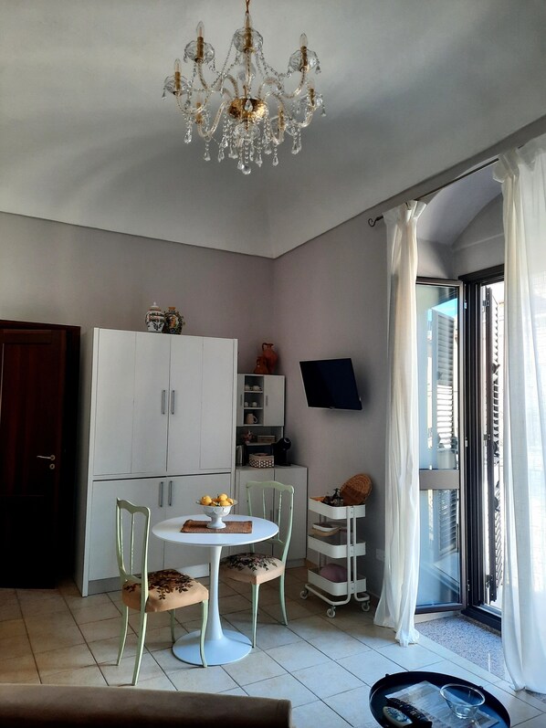 A room with a chandelier, a dining table with chairs, a cabinet, a television, and a sliding glass door.