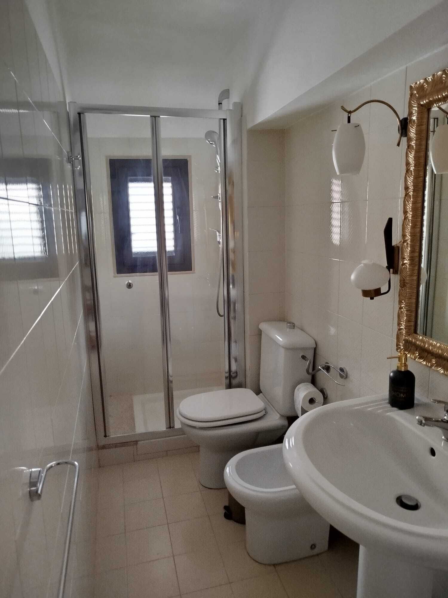 Een moderne badkamer met een douchecabine van glas, toilet, bidet en een wastafel met spiegel met gouden lijst.
