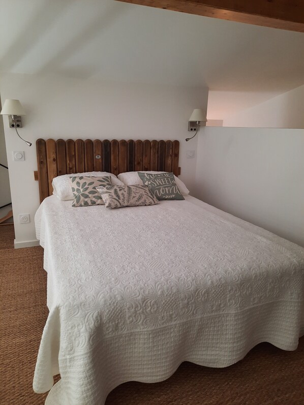 A neatly made bed with a wooden headboard, two wall-mounted lamps, and a textured white bedspread.