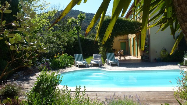 A pool area with lounge chairs, a table, and a building in the background. - Les Myrtes Studio Style Atelier (Cuers)