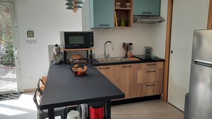 A modern kitchen with a black countertop, wooden cabinets, a stainless steel refrigerator, and a microwave. - Les Myrtes Studio Style Atelier (Cuers)