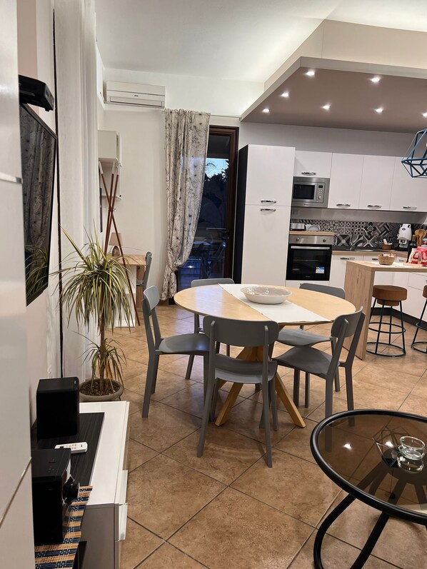 A modern kitchen with white cabinets, a microwave, and an oven. There is a dining area with a round table and chairs, and a small round table with a glass top.