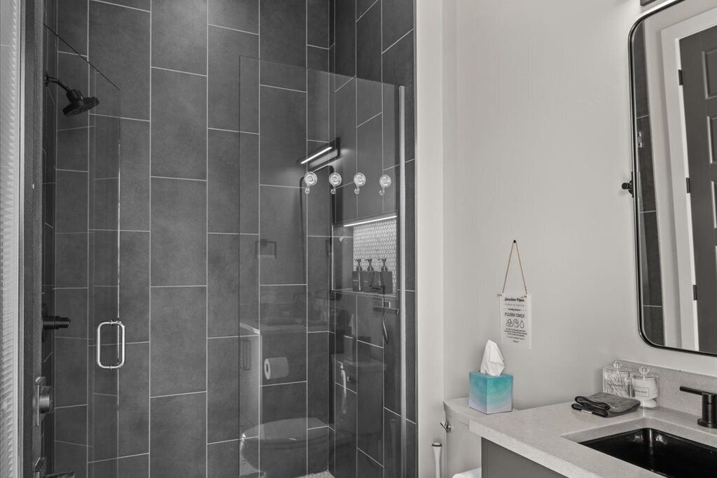 Un baño moderno con ducha de vidrio, lavamanos y espejo.