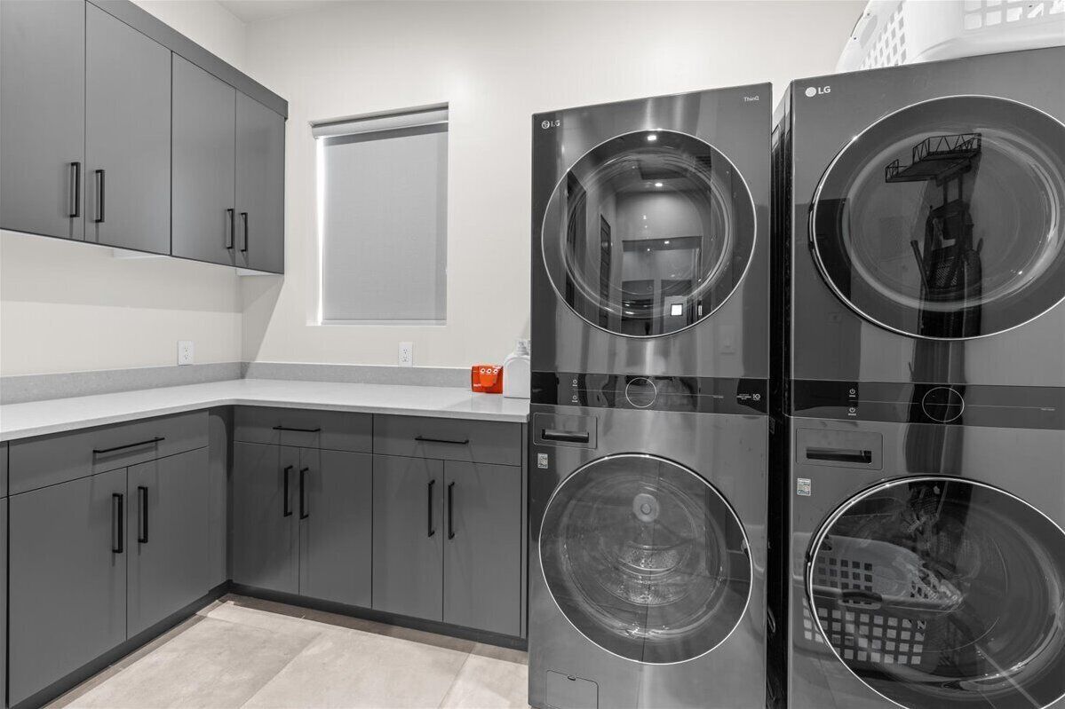 Une buanderie moderne équipée de deux machines à laver à chargement frontal en acier inoxydable et de meubles de rangement gris.