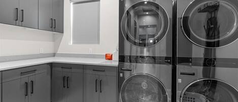 Une buanderie moderne équipée de deux machines à laver à chargement frontal en acier inoxydable et de meubles de rangement gris.