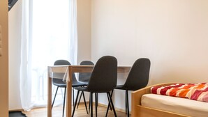 A room with a wooden bed, a small table with four chairs, and a window with curtains. - Alpen-hostel - Apartment Mittagsonne - Buxacher Straße 23 mit Motoradvermietung (Memmingen)