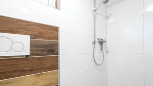 A modern bathroom with white tiles, a wooden panel wall, and a shower with a handheld showerhead. - Alpen-hostel - Apartment Mittagsonne - Buxacher Straße 23 mit Motoradvermietung (Memmingen)