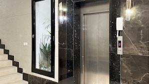 A modern elevator with a digital display, a glass door, and a marble wall.