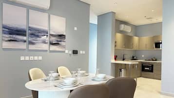 A modern dining area with a round table set for four, a kitchen with stainless steel appliances, and a grey wall with three abstract paintings.