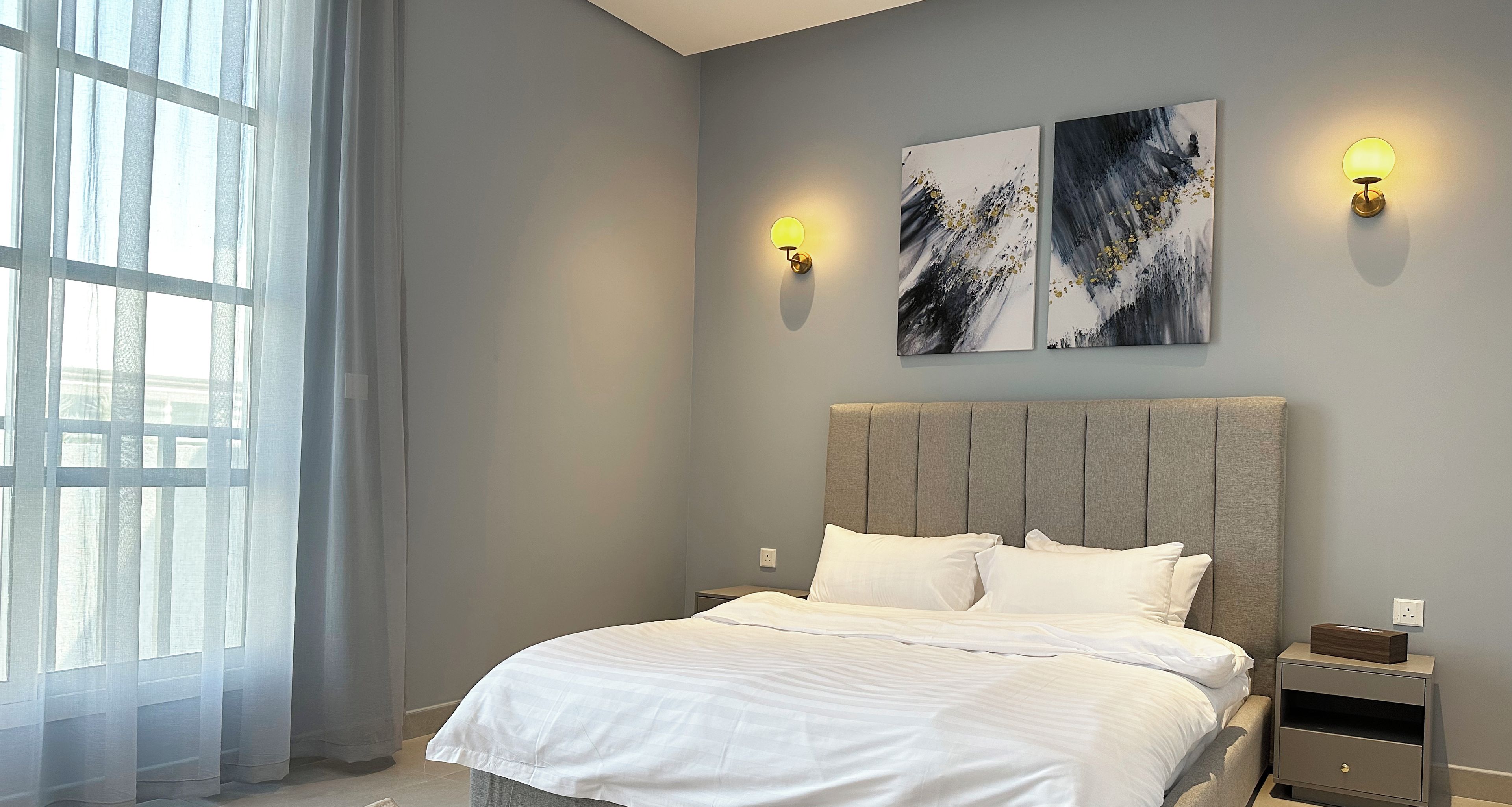 Un dormitorio moderno con una cama grande, dos luces fijadas a la pared y arte abstracto en la pared.