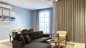 Una sala de estar moderna con un sofá modular, una mesa de centro y un televisor. Hay un comedor con una mesa y sillas, y un ventanal con cortinas.