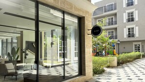 Una entrada de hotel moderna con puertas de vidrio grandes, un área de estar con sillas y una mesa, y un letrero afuera.