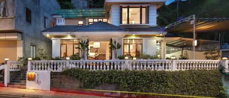 Un hotel de dos pisos con balcón, entrada cubierta y fachada bien iluminada.