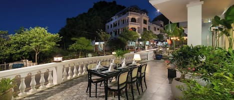 An outdoor dining area with a tiled floor, a table set for six, and potted plants.