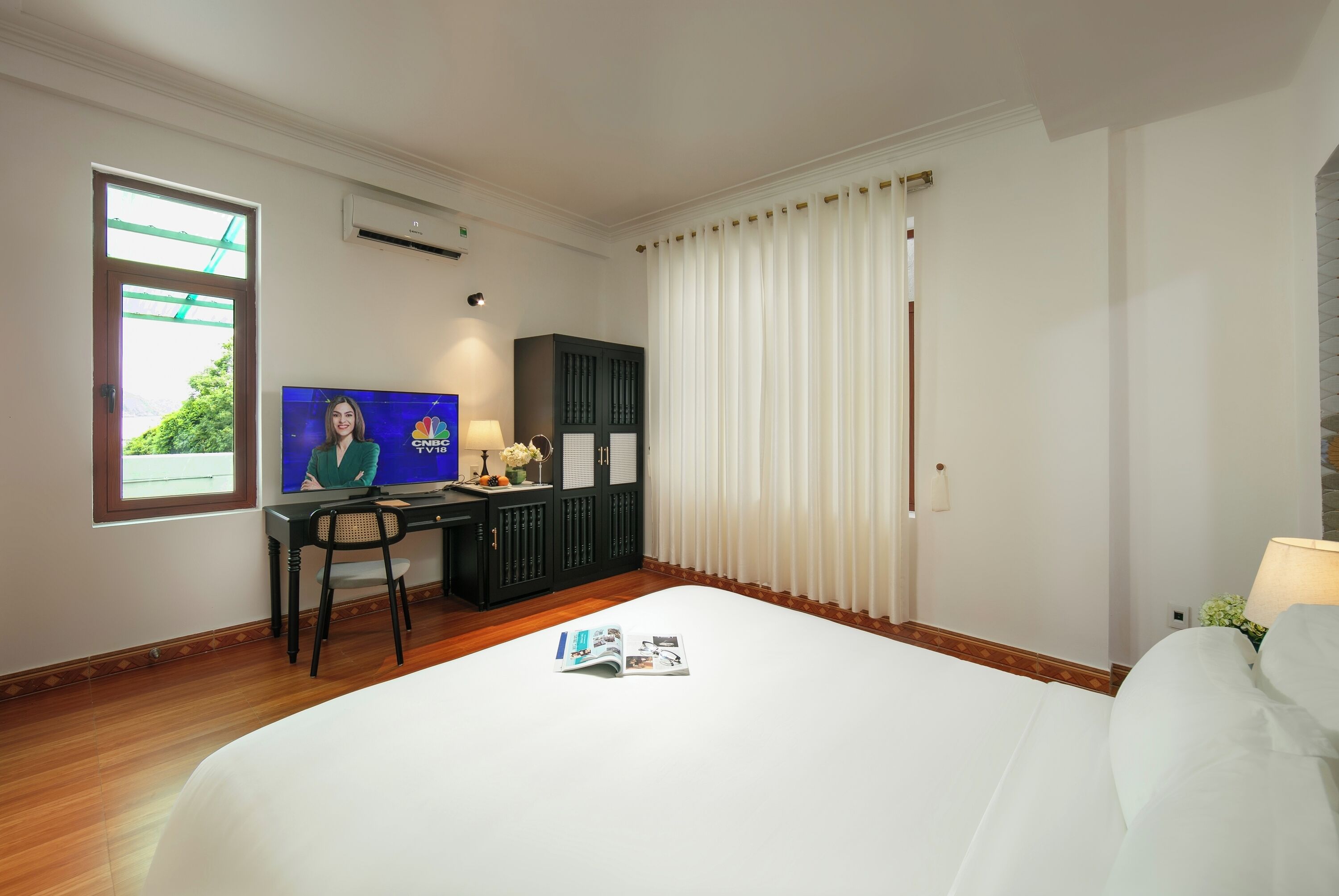 A hotel room with a bed, a desk with a TV, a chair, a cabinet, and a window with curtains.