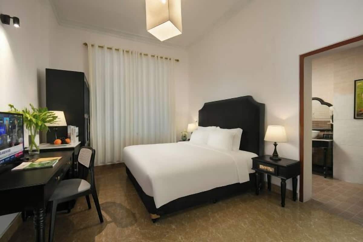 Een hotelkamer met een bed, een bureau met een computer, een stoel, een lamp en een raam met gordijnen.