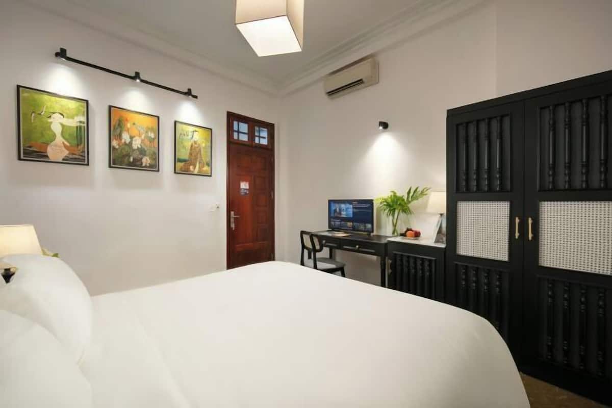Een hotelkamer met een bed, bureau, computer en kunstwerk aan de muur.