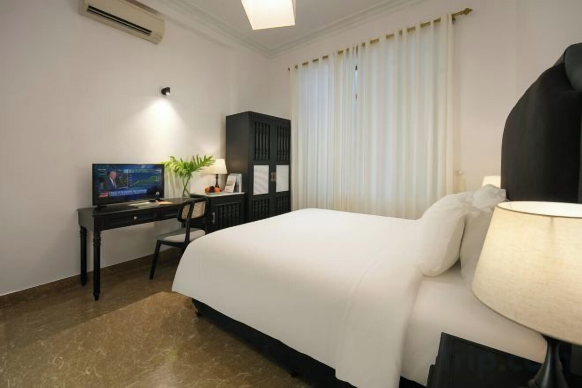A hotel room with a bed, a desk with a computer, a lamp, and a window with curtains.