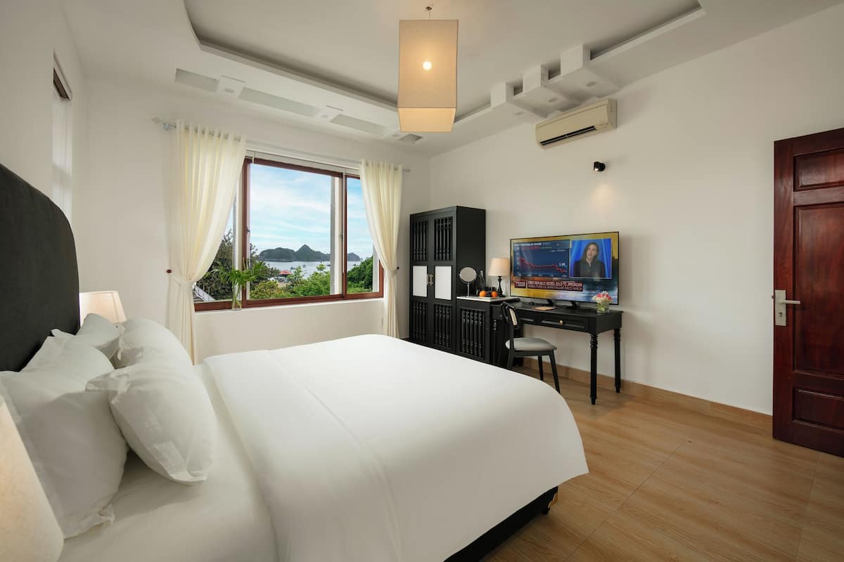 Een hotelkamer met een groot bed, een bureau met een computer, een televisie en uitzicht op het omliggende landschap.