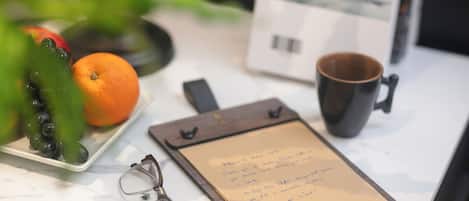 A clipboard with handwritten notes, a mug, a plate with fruits, and a pair of glasses on a table.