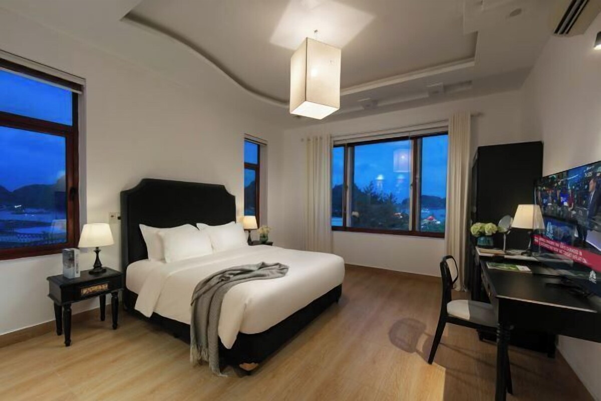A hotel room with a large bed, a desk, and a view of the cityscape.