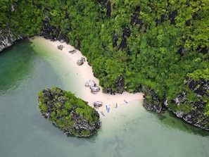 An aerial view of a secluded beach with clear turquoise waters, surrounded by dense green forest and rocky outcrops.