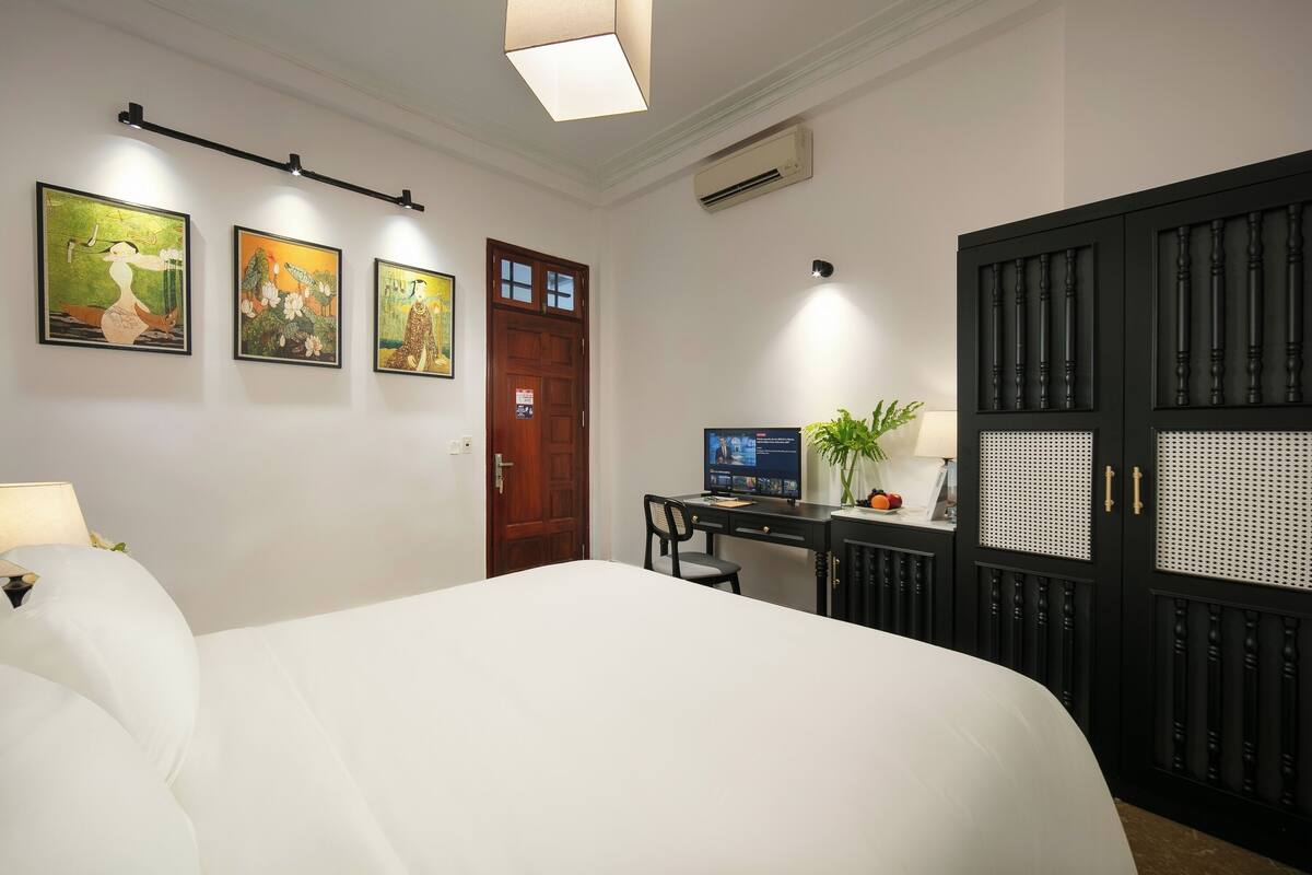 Een hotelkamer met een bed, bureau, computer en kunstwerk aan de wand.