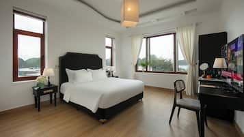 A hotel room with a large bed, a desk, and a TV. There are windows with curtains and a view of the mountains.