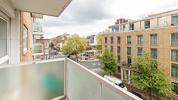 Un immeuble d’habitation doté de nombreuses fenêtres, d’un balcon et donnant sur la rue, avec vue sur des arbres et d’autres bâtiments.