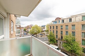 Un edificio residencial con varias ventanas, un balcón y vista a la calle con árboles y otros edificios.