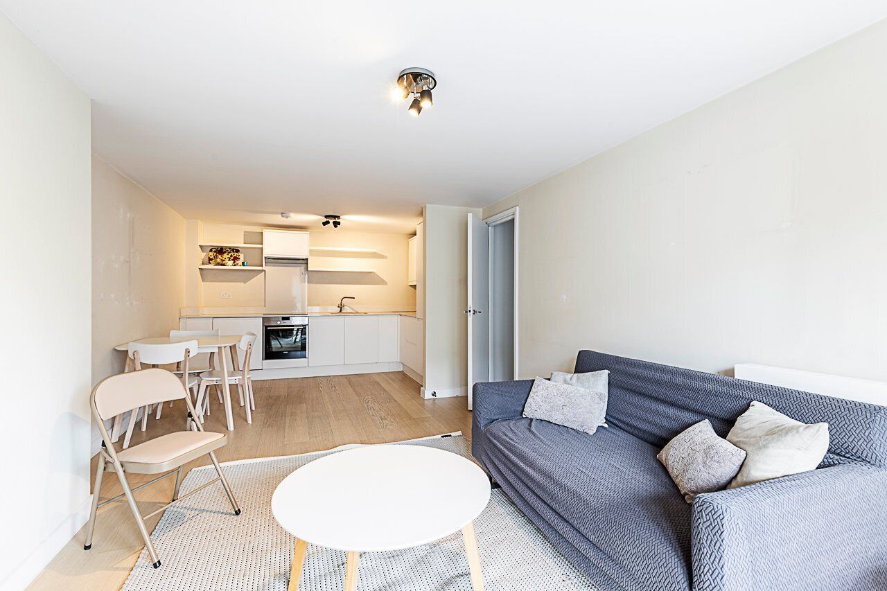 Una sala de estar moderna con un sofá gris, una mesa de centro blanca y una cocina al fondo.