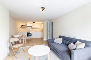 Una sala de estar moderna con un sofá gris, una mesa de centro blanca y una cocina al fondo.