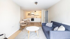 Un salon moderne avec un canapé, une petite table ronde et une cuisine en arrière-plan.