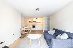 A modern living room with a sofa, a small round table, and a kitchen in the background.
