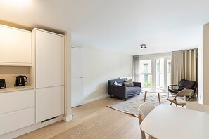 Una sala moderna con un sofá, una mesa de centro y una mesa de comedor. Hay un armario y una puerta que da a otra habitación.