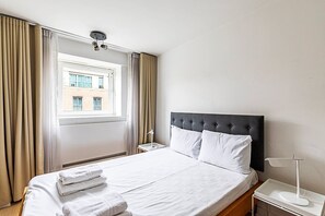 Une chambre d’hôtel avec un lit, une table de chevet, une lampe et une fenêtre avec des rideaux.