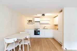 Una cocina compacta con armarios blancos, horno empotrado y comedor con mesa y sillas blancas.