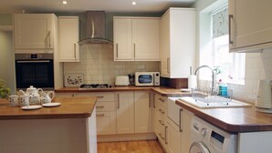 A modern kitchen with white cabinets, a microwave, a sink, and a washing machine. - Country Hideaways | Cobblestone Cottage | Ripon (Ripon)