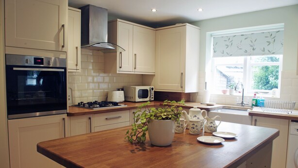 A modern kitchen with white cabinets, a wooden countertop, a built-in oven, a microwave, and a window with a view of greenery. - Country Hideaways | Cobblestone Cottage | Ripon (Ripon)