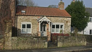A stone cottage with a tiled roof, a central door, and two windows with shutters. - Country Hideaways | Cobblestone Cottage | Ripon (Ripon)