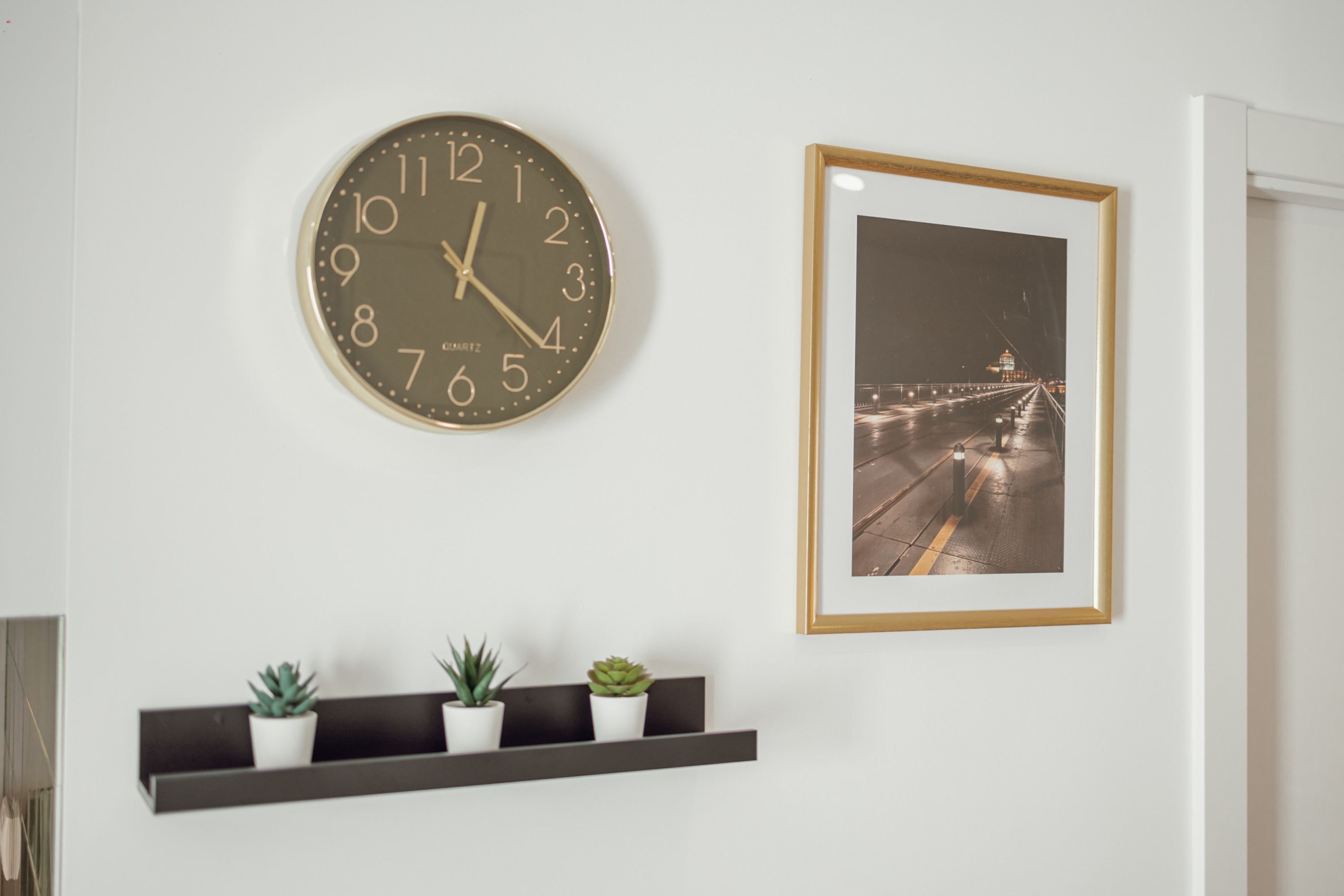 Une horloge murale, une photographie encadrée et trois plantes en pot, disposées sur une étagère.