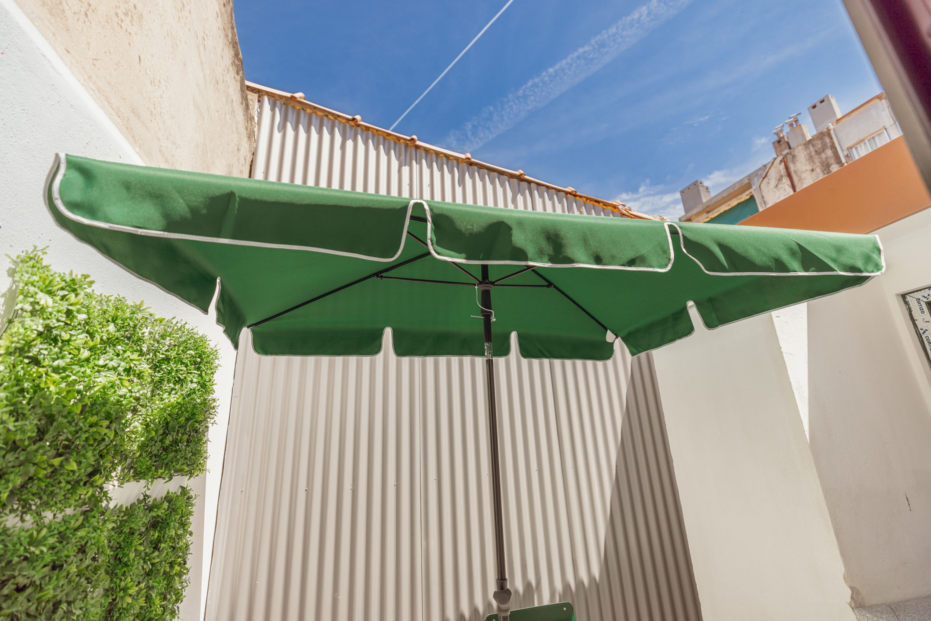 A green umbrella attached to a corrugated metal wall.